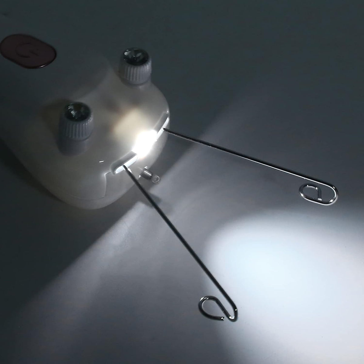 A close-up of a threading facial hair removal device with two gray knobs and a bright built-in light, with two long metal wire loops extending from it, photographed on a dark gray surface.