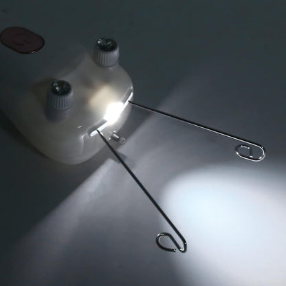 A close-up of a threading facial hair removal device with two gray knobs and a bright built-in light, with two long metal wire loops extending from it, photographed on a dark gray surface.